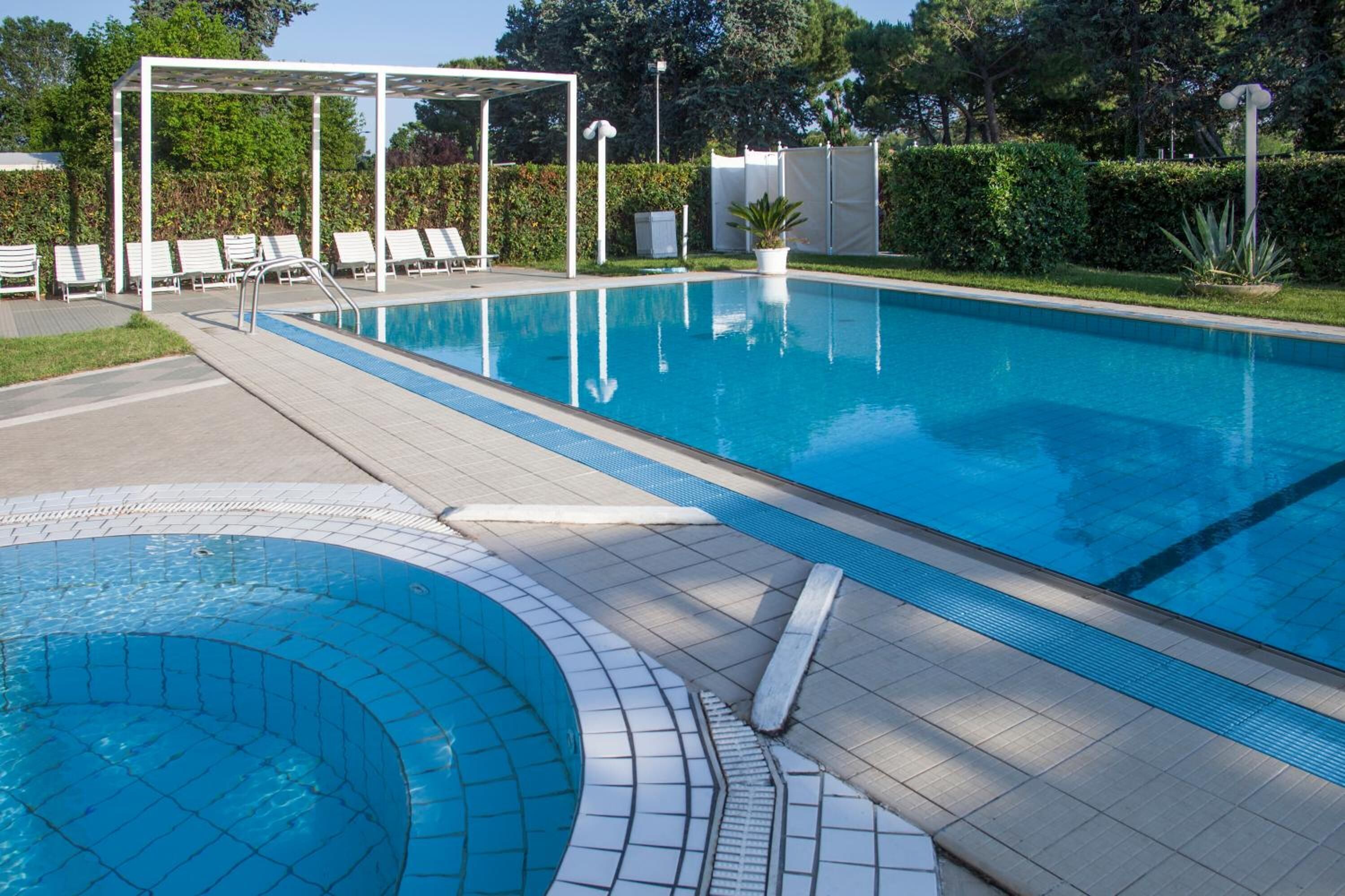 A swimming pool with a sun deck, lounge chairs, and a covered seating area.