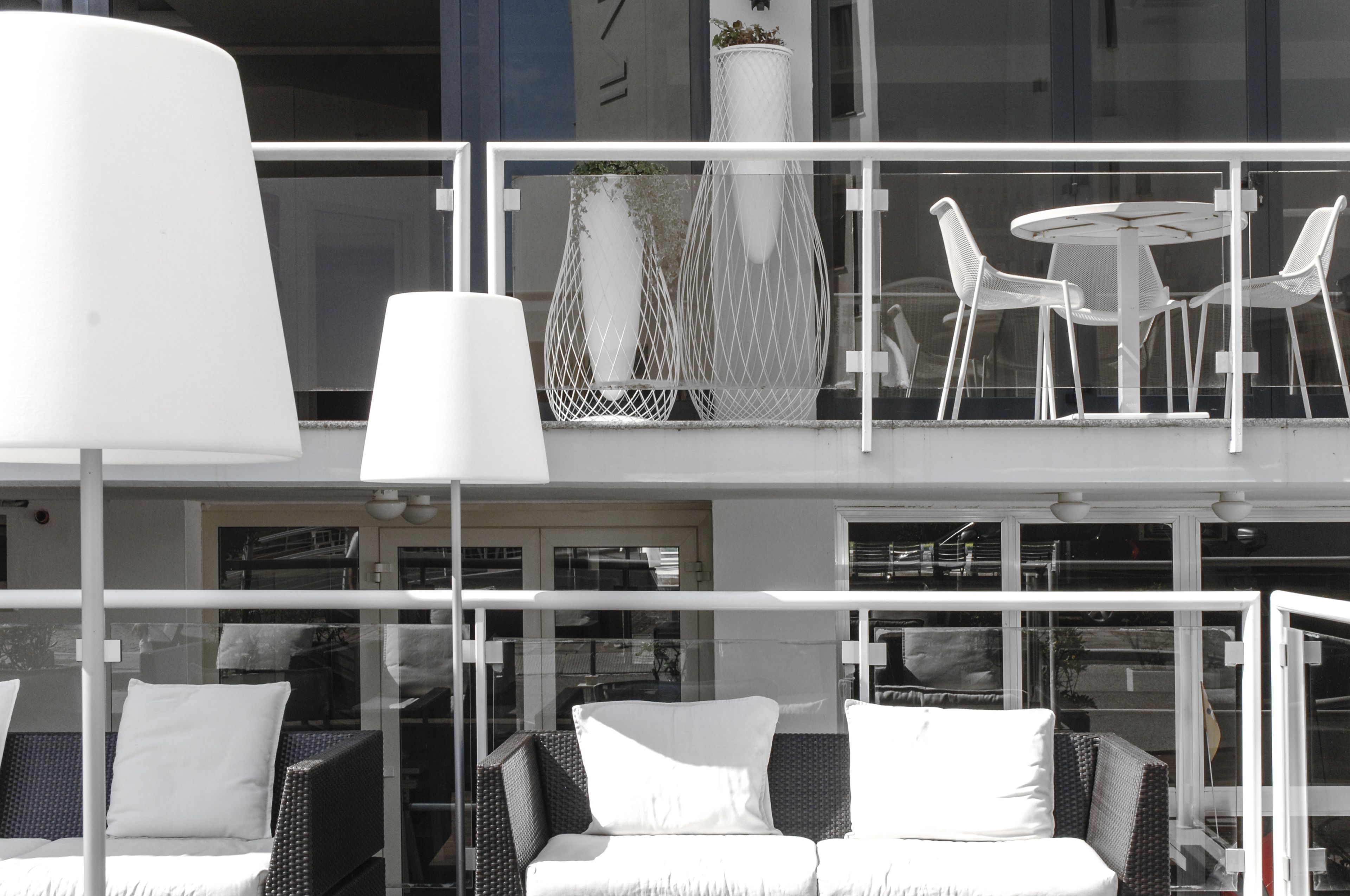 Un balcon agrémenté de meubles en osier, de coussins blancs et d’une table blanche avec des chaises.