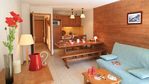 A cozy living room with a wooden sofa, a dining table with chairs, a kitchen area with wooden cabinets, and a wooden wall.