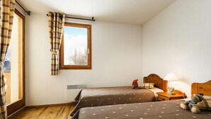 A room with two beds, a window with curtains, a nightstand with a lamp, and a teddy bear on the right bed.
