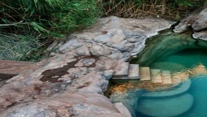 Une source d’eau chaude naturelle, avec une plateforme en bois et des marches menant à l’eau.