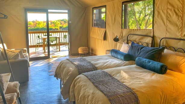 Un hébergement sous tente comprenant deux lits, un balcon avec des chaises et une vue sur la verdure.