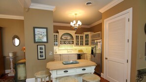 A kitchen with white cabinets, a central island with stools, a chandelier, and a refrigerator.