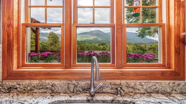 Een badkamer met een groot raam, een wastafel en uitzicht op een bergachtig landschap.