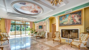 A grand lobby with marble flooring, ornate chairs, a fireplace, and a large mural. - Venera & Anastasia Palace Apartments (Sunny Beach)
