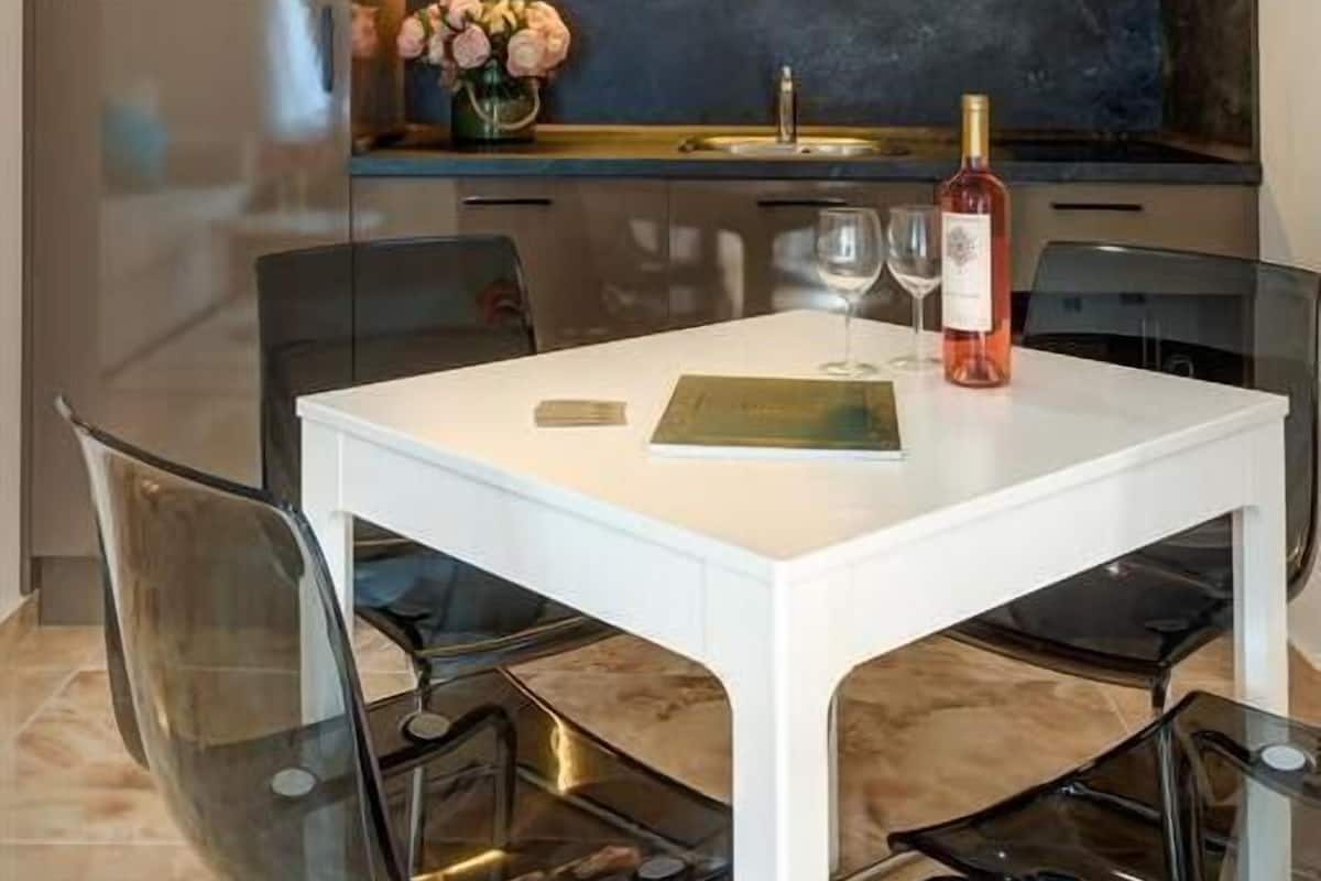 A modern kitchen with a white dining table, clear chairs, and a wine bottle on the table.