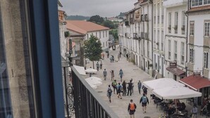 Une rue piétonne bordée de bâtiments des deux côtés, avec des espaces de restauration en plein air et une balustrade donnant sur la rue.