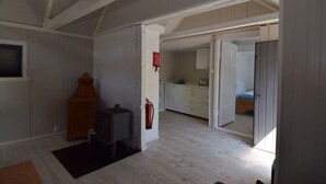 Une pièce spacieuse avec un haut plafond, une cheminée, une petite table et une porte donnant sur un coin cuisine.