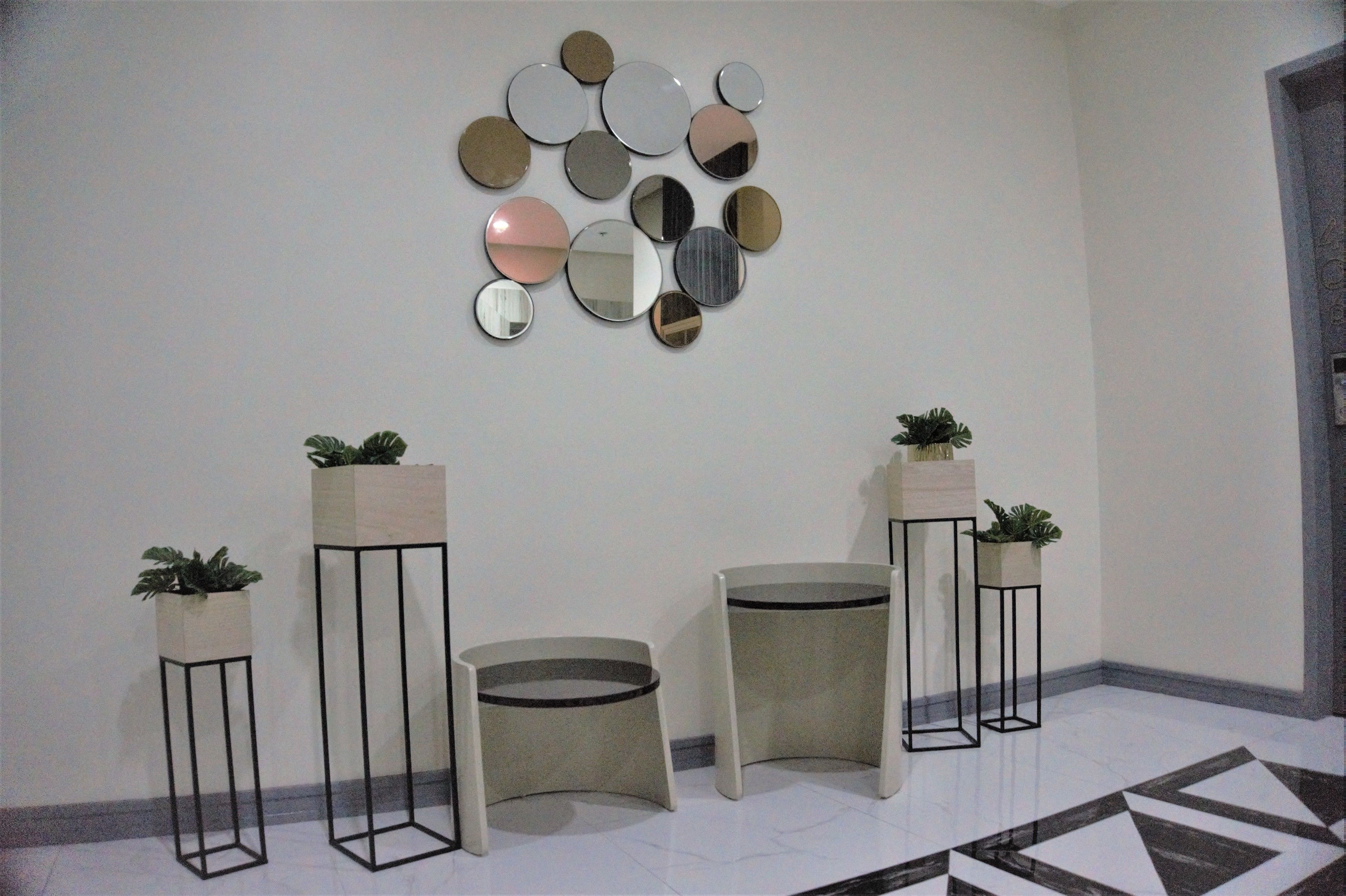 A hallway with a wall-mounted mirror arrangement, potted plants, and a geometric patterned floor.