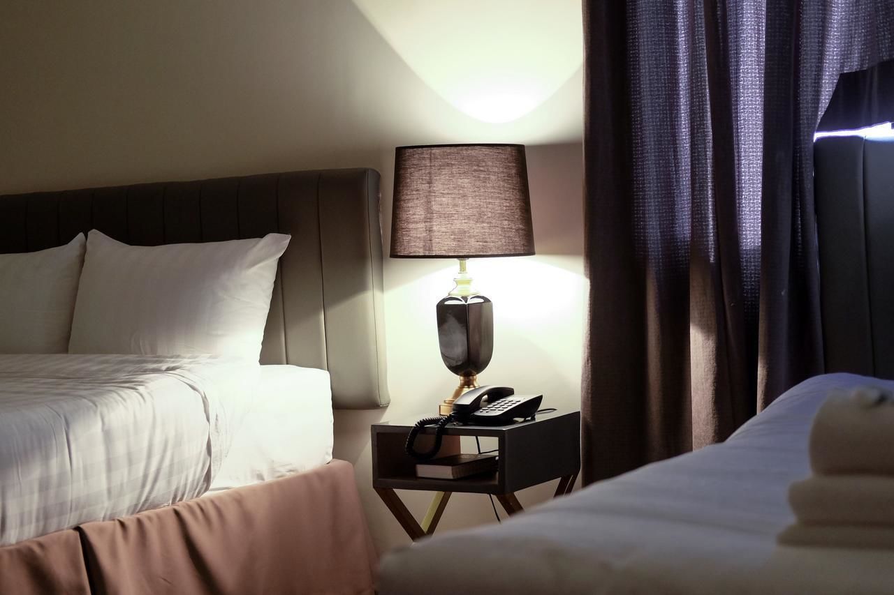 A hotel room with a bed, a bedside table with a lamp, and a window with curtains.