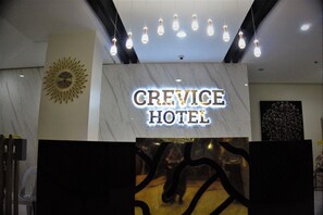 Exterior del Hotel Crevice, con fachada de mármol, un diseño en forma de sol en la pared y una lámpara moderna sobre la entrada.