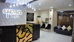A hotel reception area with a marble reception desk, black and gold decor, a black sofa with pillows, and a wall-mounted air conditioner. - Crevice Hotel (Davao)
