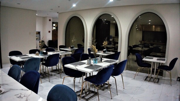 A dining area with tables and chairs, arched windows, and a view of the kitchen. - Crevice Hotel (Davao)