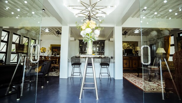 Un interior modern amb una taula central, dos tamborets, una escala i una làmpada decorativa al sostre.