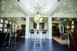 Un intérieur moderne avec une table centrale, deux tabourets de bar, une échelle et un luminaire décoratif au plafond.
