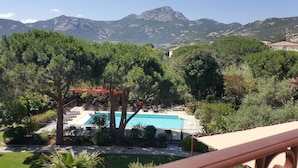 Área de piscina com espreguiçadeiras e guarda-sóis, cercada por árvores e montanhas ao fundo.