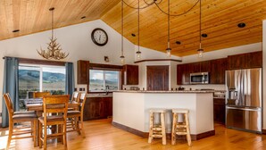 A spacious kitchen with wooden cabinets, a large island with stools, a built-in microwave, and a stainless steel refrigerator. - Yellowstone Trail - Great Home Overlooking the Yellowstone River (Pray)
