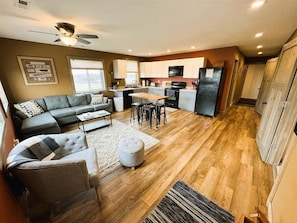A spacious living room with a sofa, ottoman, and coffee table, a kitchen with modern appliances, and a dining area with chairs.