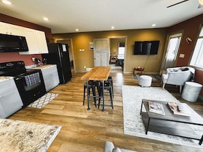 A modern kitchen with a dining area, wooden flooring, and a living space with a sofa and coffee table.
