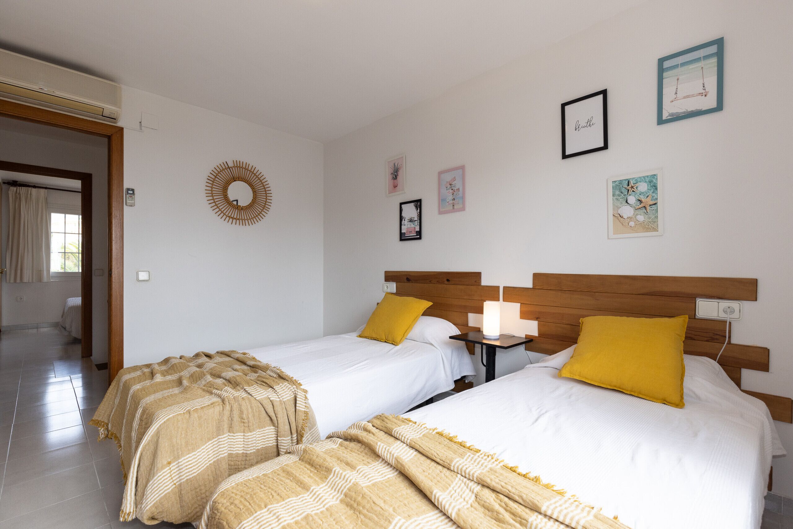 Hotelkamer met twee bedden, een houten hoofdbord, een klein nachtkastje met een lamp, en wanddecoraties waaronder ingelijste foto’s en een ronde spiegel.