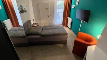 Une chambre moderne avec un canapé-lit, un téléviseur fixé au mur et une fenêtre avec des rideaux.