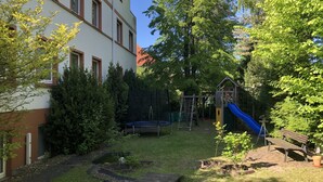 Ein Wohngrundstück mit Spielbereich, einschließlich Rutsche und Klettergerüst, umgeben von Bäumen und einem Gebäude.