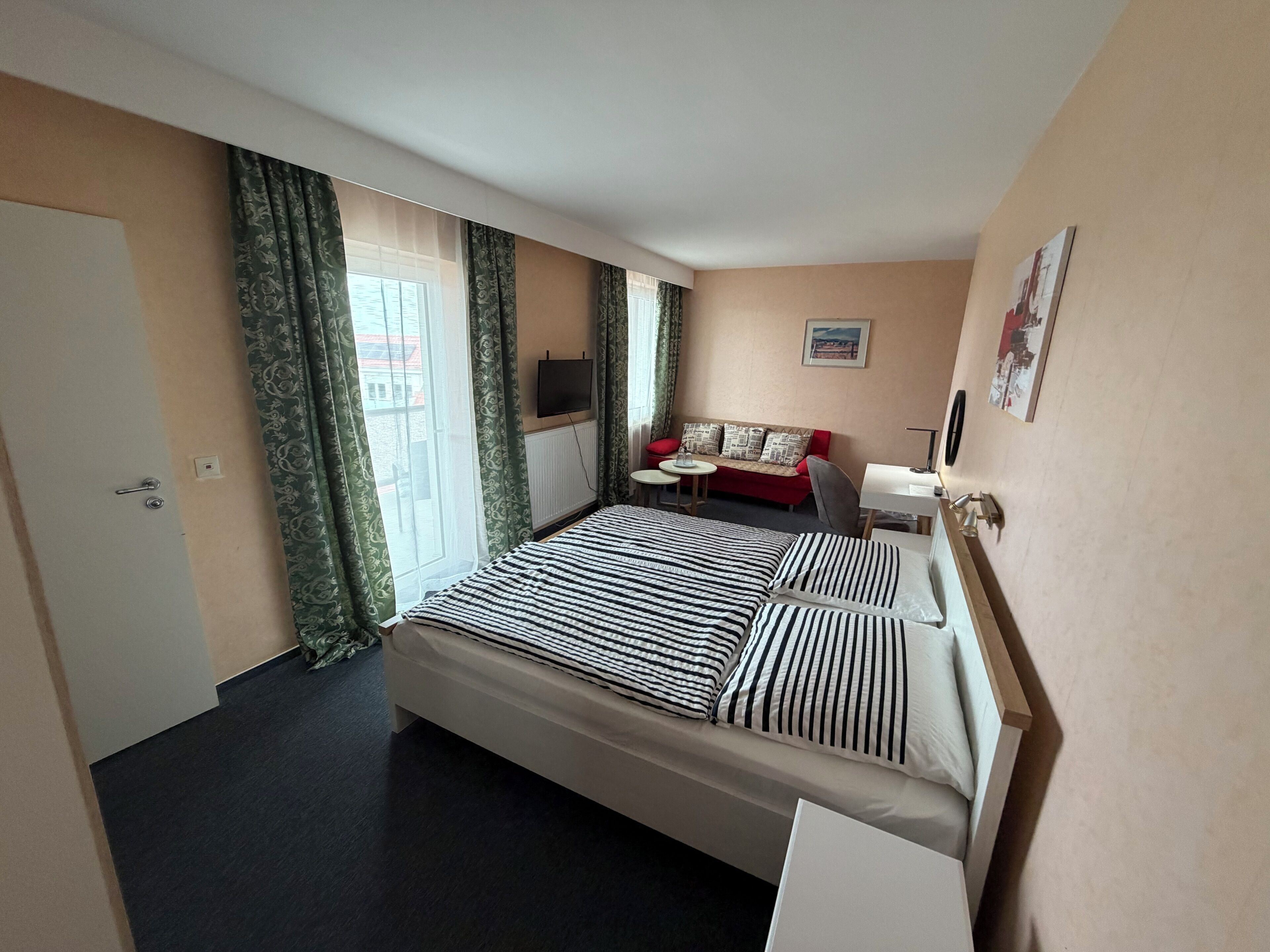 Habitación de hotel con cama, sofá, televisión y ventana con cortinas.