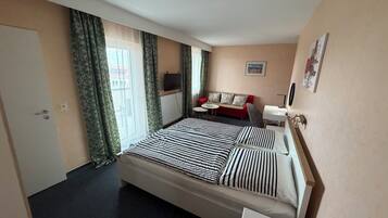 Habitación de hotel con cama, sofá, televisión y ventana con cortinas.