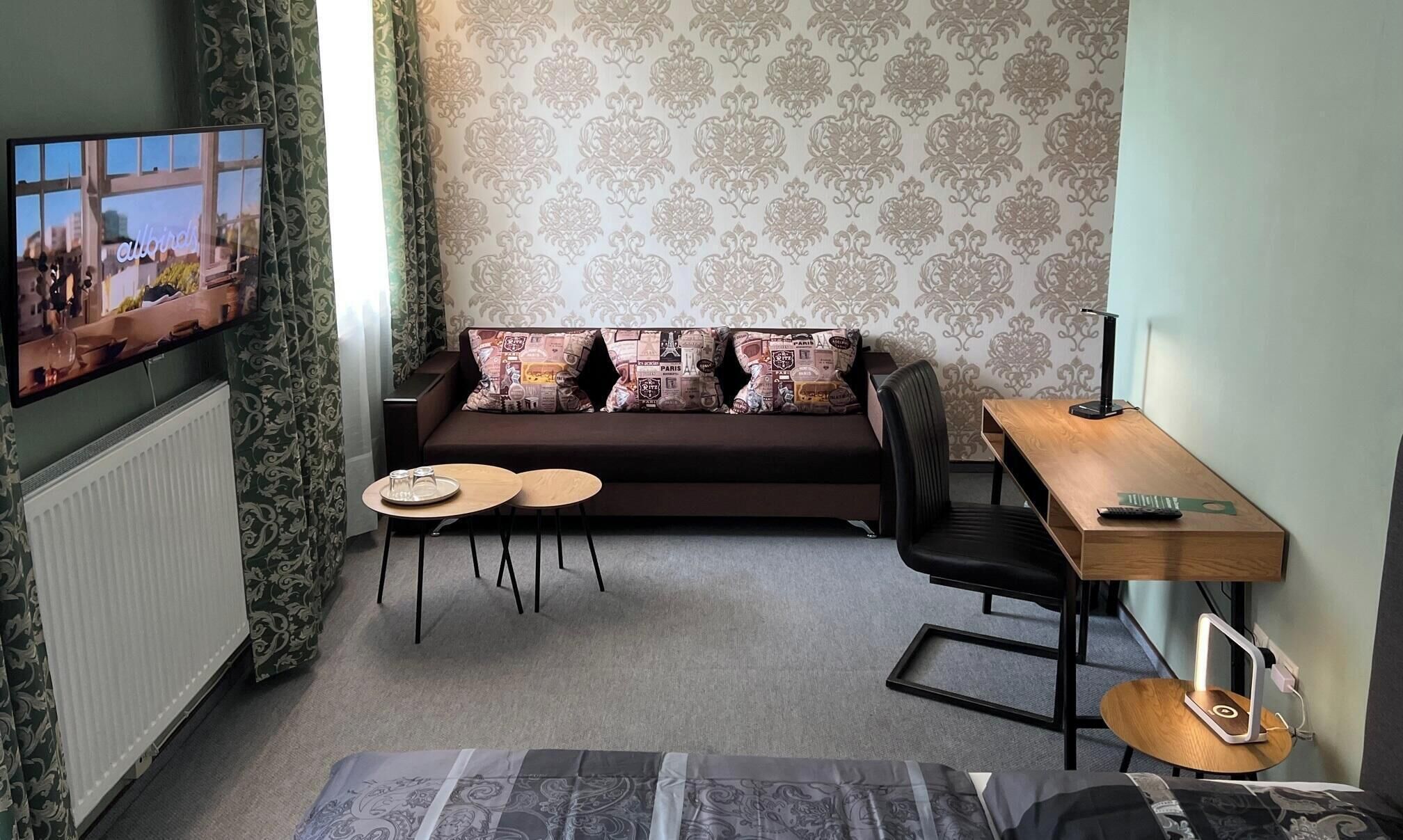 Ein Wohnzimmer mit einer Couch, zwei kleinen Tischen, einem Fernseher und einem Schreibtisch mit einer Lampe.