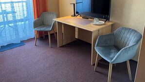 Ein Hotelzimmer mit Schreibtisch, zwei Stühlen, Fernseher und einem fenster mit Vorhängen.