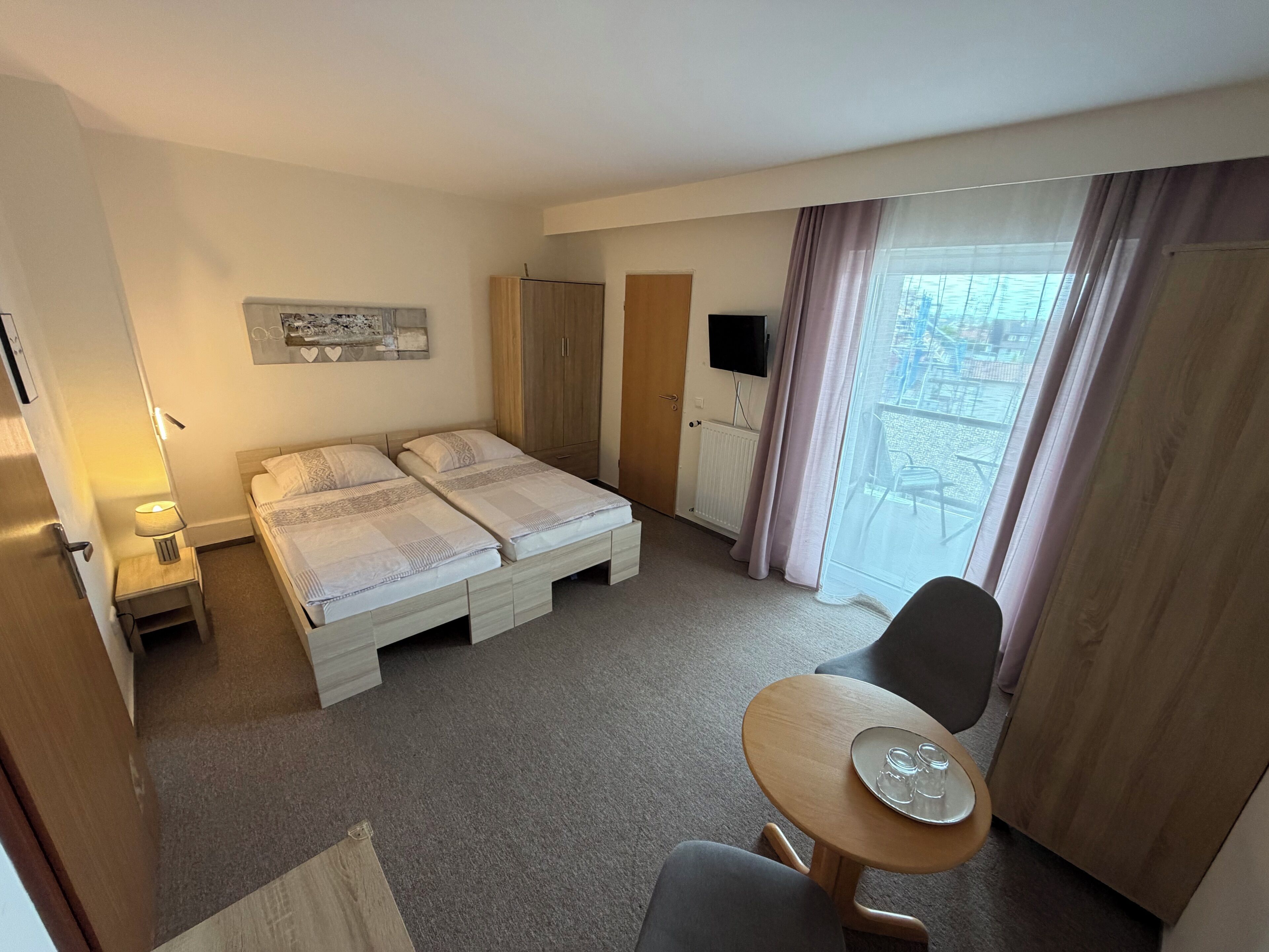 Habitación de hotel con dos camas, televisión, una mesa con vasos y vista al exterior.