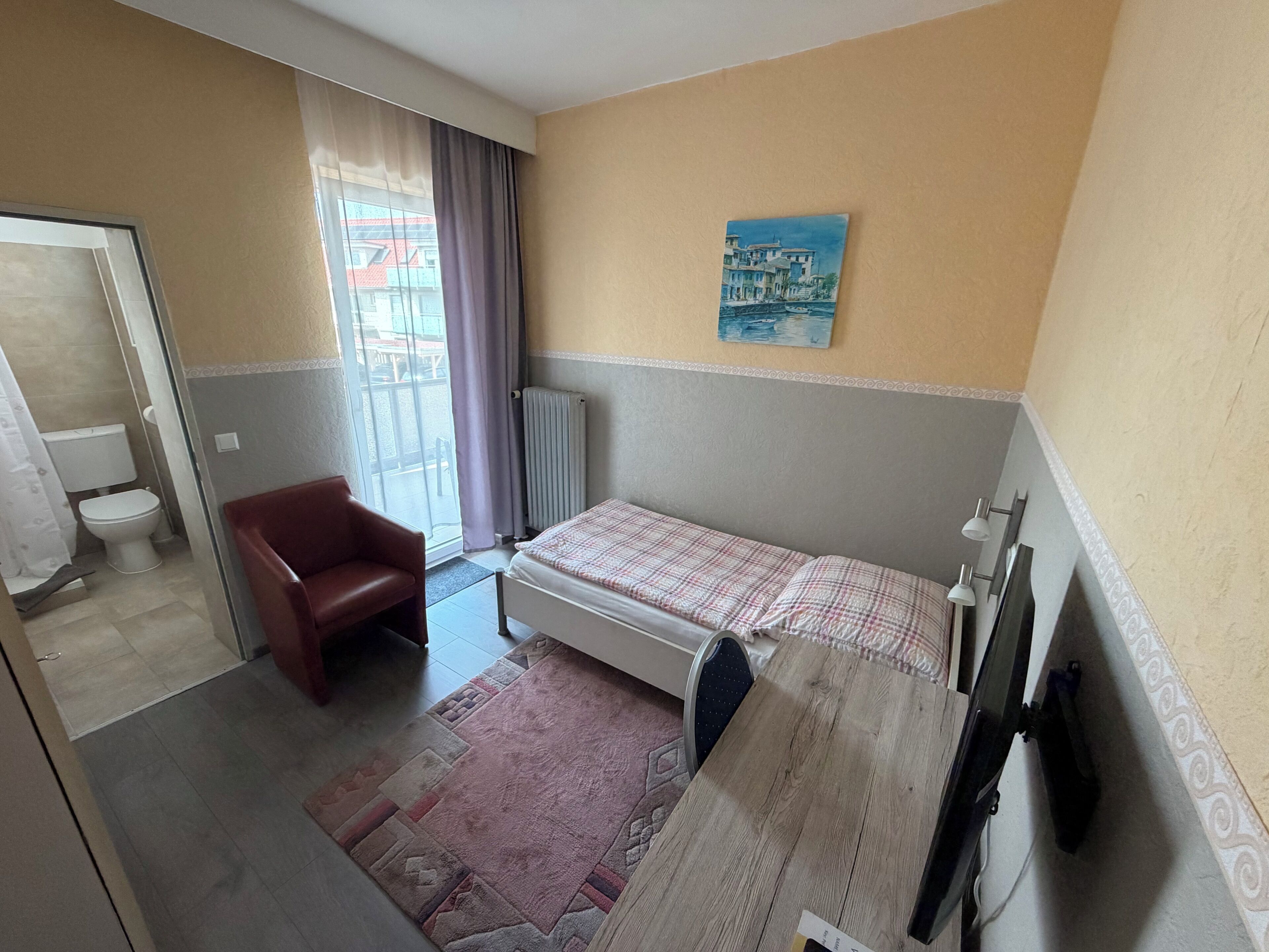 Una habitación de hotel con cama, una silla, un radiador y un cuadro en la pared.