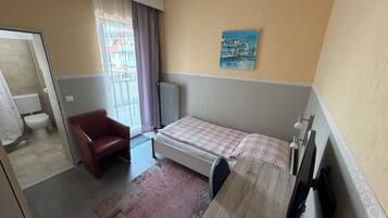 Una habitación de hotel con cama, una silla, un radiador y un cuadro en la pared.