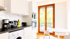 Eine kompakte Küche mit Waschmaschine, Kaffeemaschine und Toaster. Es gibt eine Essecke mit Tisch und Stühlen sowie eine Glastür, die zu einem Außenbereich führt.
