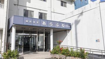 A building entrance with a covered entryway, a sign with Japanese characters, and potted plants.
