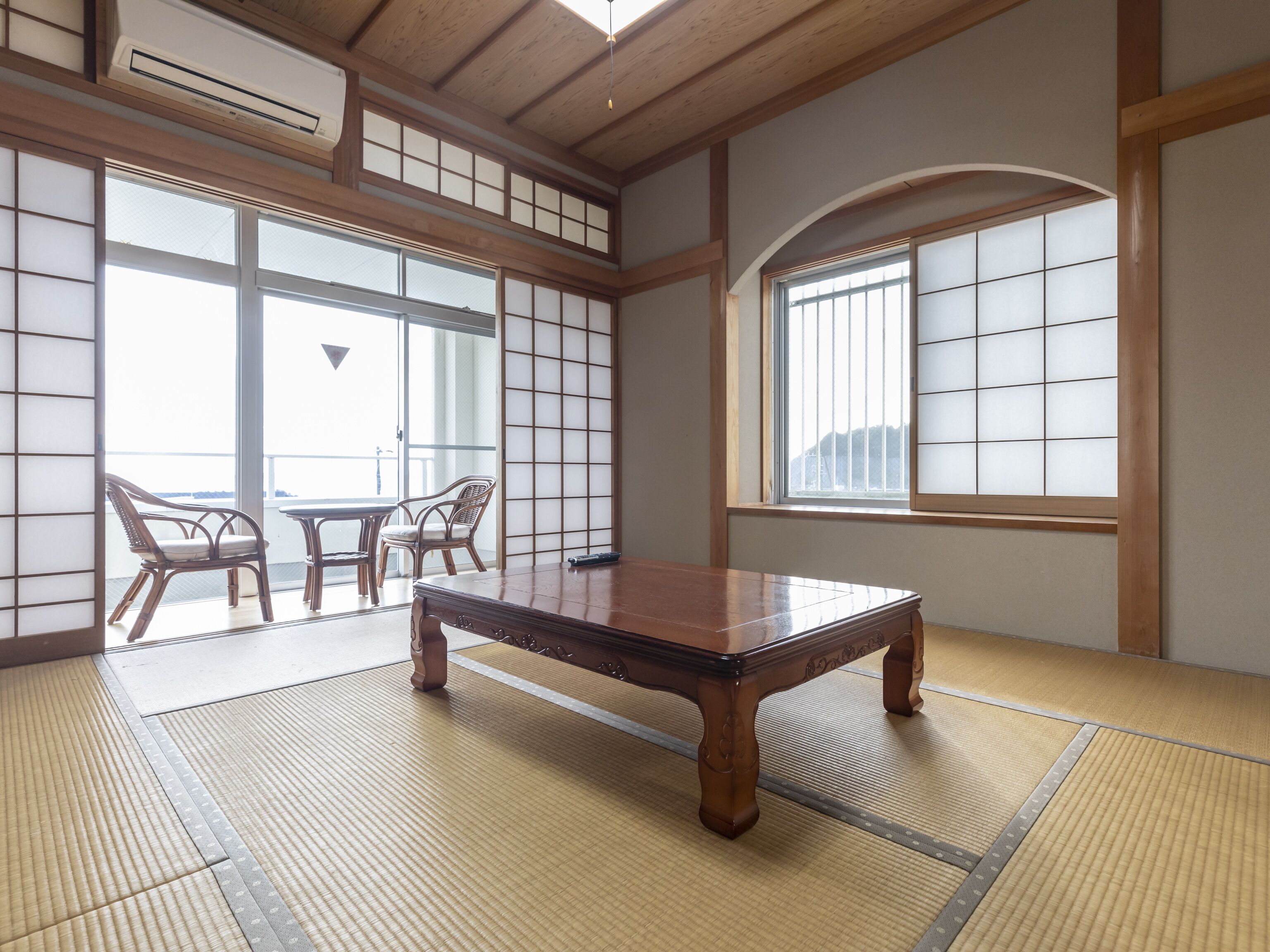A tatami mat room with a low wooden table, two chairs, and large windows with shoji screens.