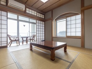 A tatami mat room with a low wooden table, two chairs, and large windows with shoji screens. - Arafune Resort (Kushimoto)