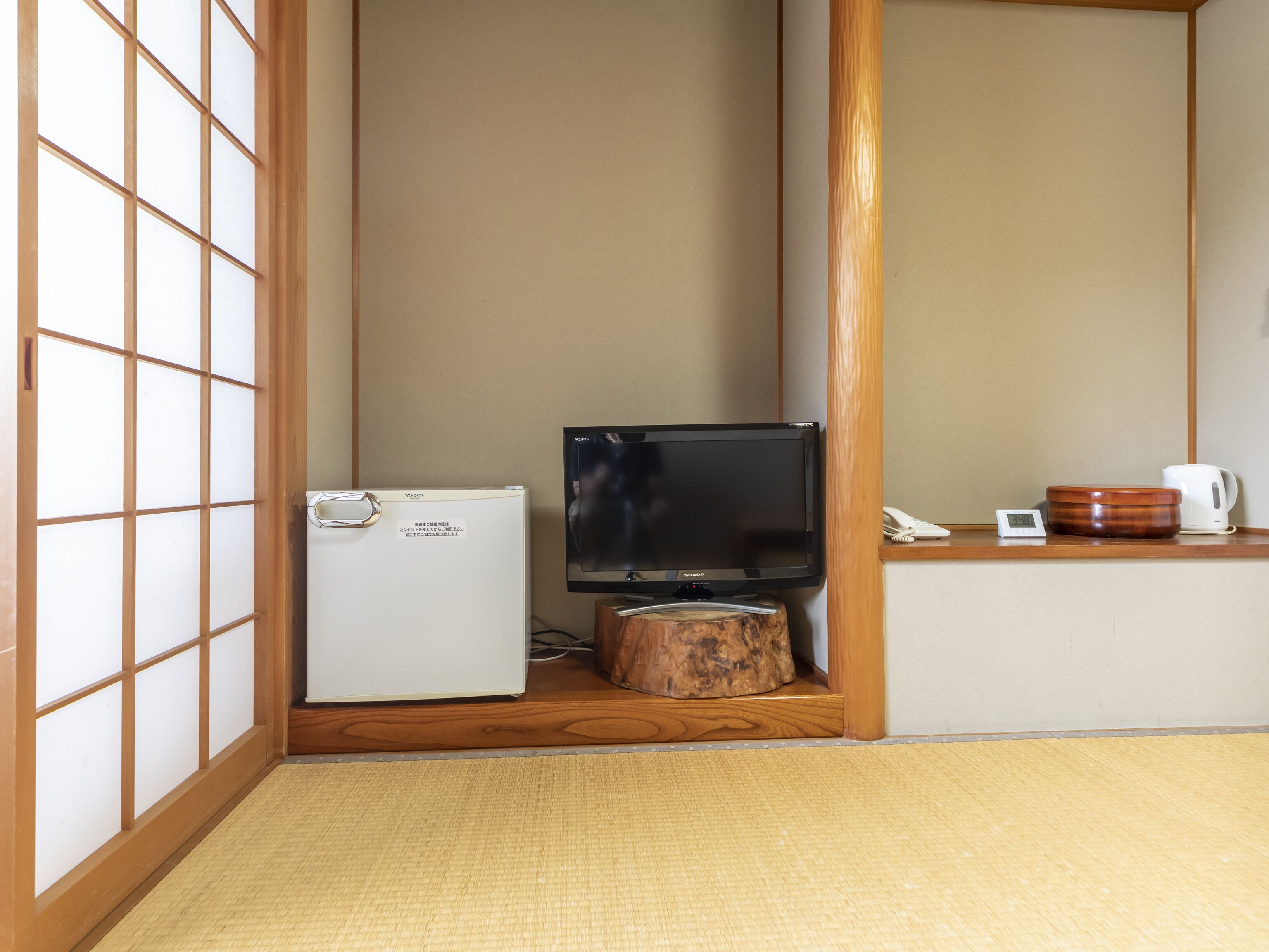 A room with a television, a small refrigerator, a wooden coffee table, and a traditional Japanese shoji screen.