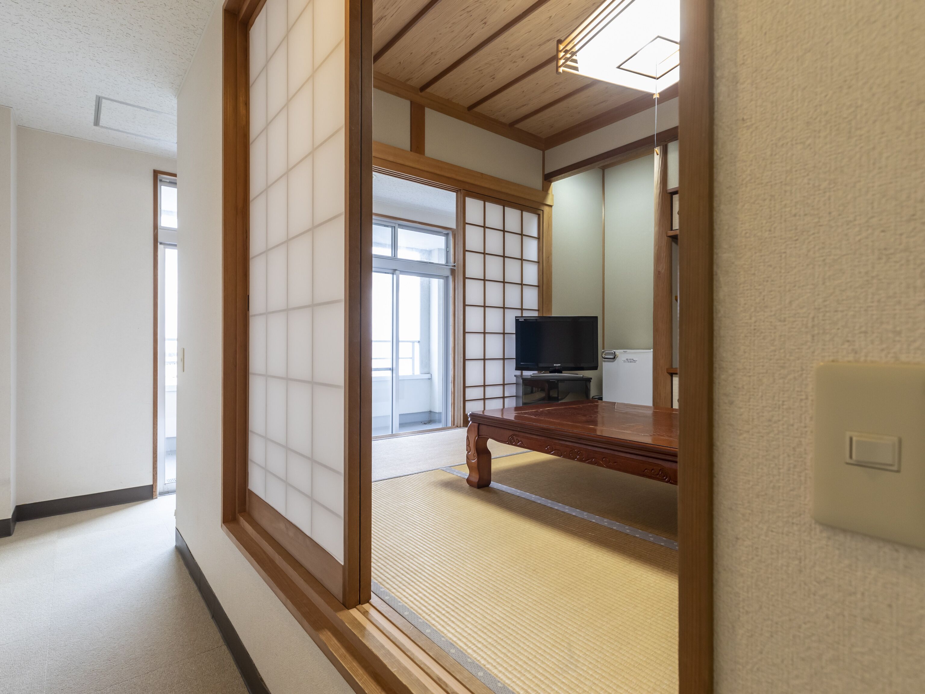 A traditional Japanese room with tatami flooring, a sliding shoji screen, a wooden desk, and a television.