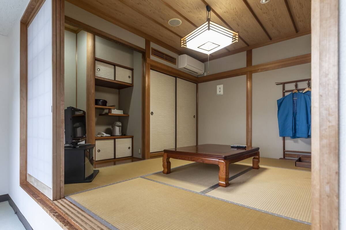 Una habitación japonesa tradicional con suelo de tatami, una mesa de madera, un televisor y un armario.