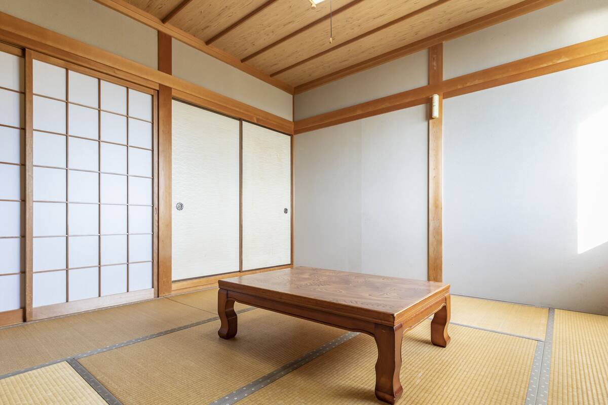 Una habitación japonesa tradicional con suelo de tatami, una mesa de madera baja, puertas correderas shoji y techo de madera.