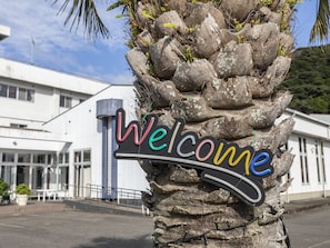 A 'Welcome' sign attached to a palm tree in front of a building. - Arafune Resort (Kushimoto)