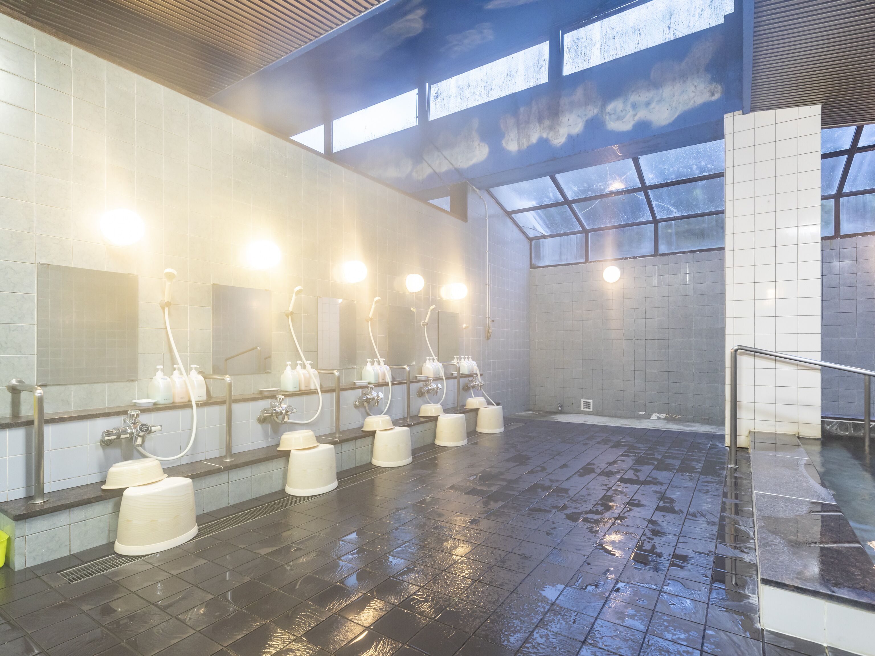 Een openbaar toilet met meerdere wastafels, handdrogers en een betegelde vloer.