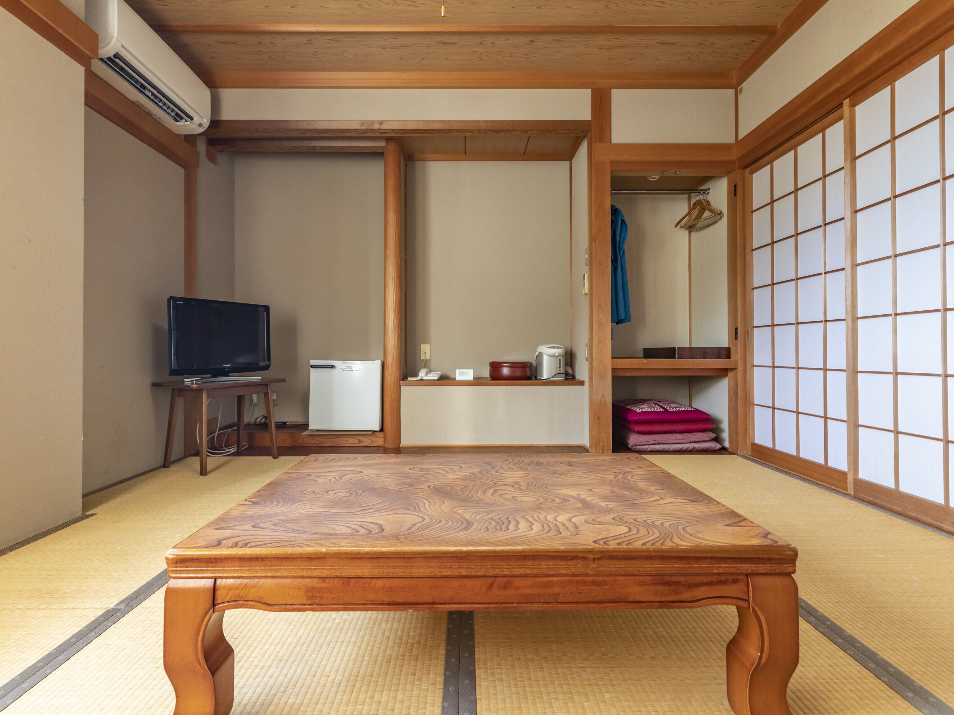 A traditional Japanese room with tatami flooring, a wooden table, a television, a refrigerator, and a sliding door with a grid pattern.