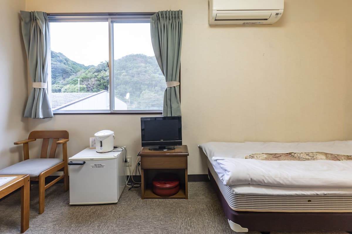 Habitación de hotel con una cama, un escritorio con computadora, una silla, un refrigerador pequeño y una ventana con cortinas.