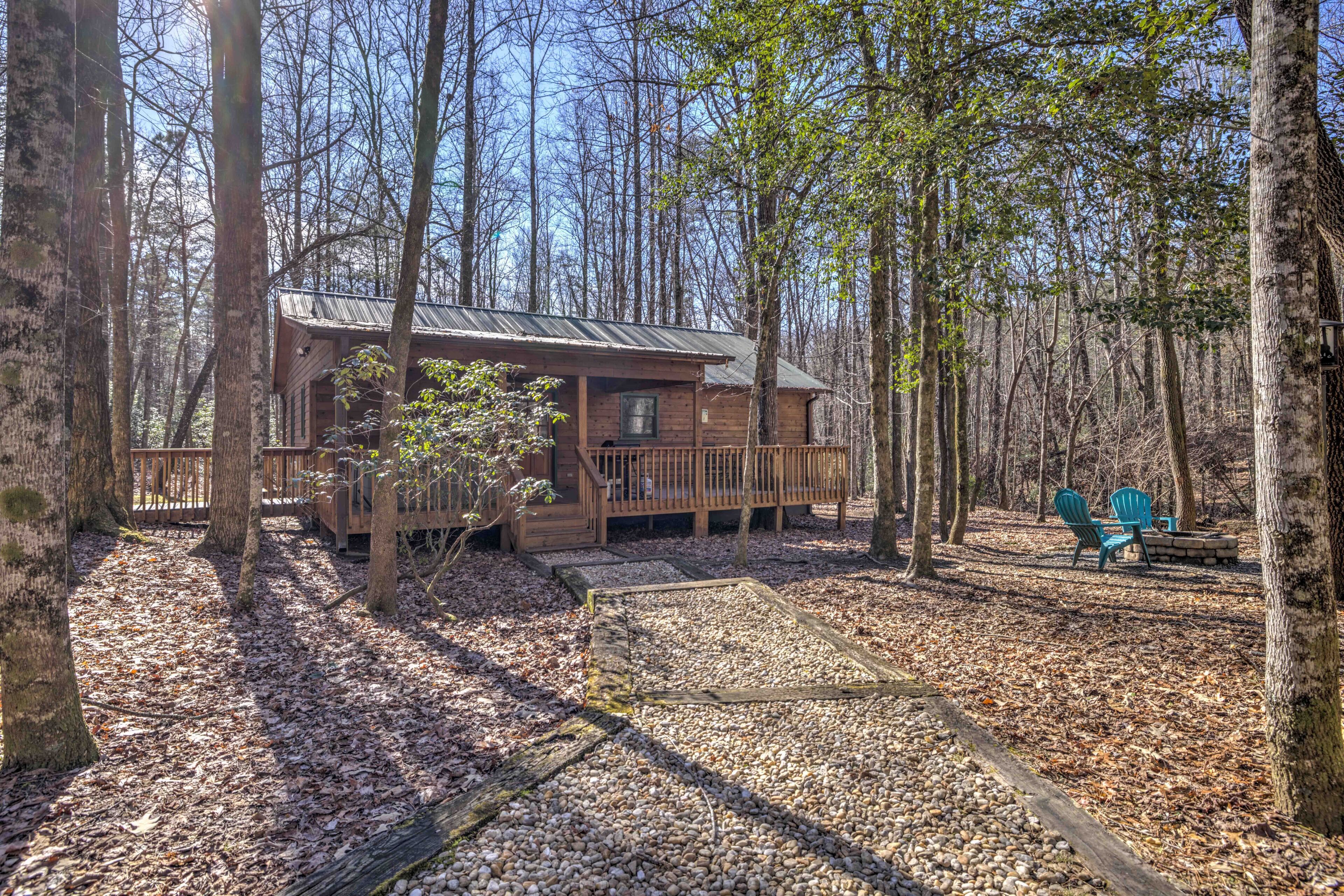 A cabin with a wooden deck, surrounded by trees and a gravel path.