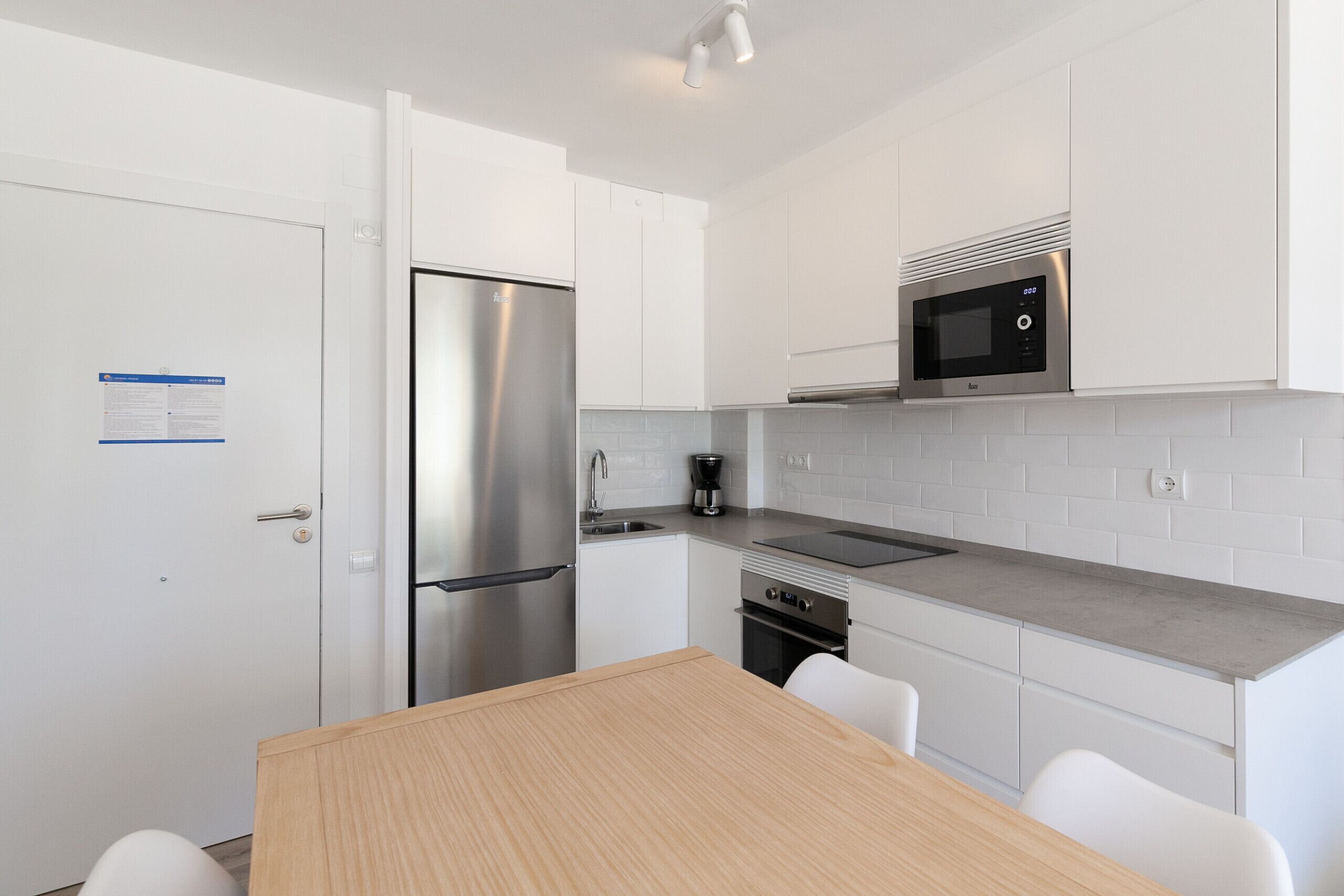 Una cocina moderna con gabinetes blancos, electrodomésticos de acero inoxidable y una mesa de madera.