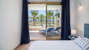 A hotel room with a bed, a nightstand, a lamp, and a view of a pool and palm trees. - Beachfront Apartment · AirCon · WiFi · Pool UHC NOVELTY 010 (Salou)