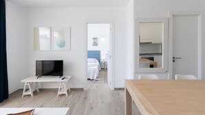 A modern hotel room with a flat-screen TV, a wooden dining table, and a bed with a blue headboard. - Beachfront Apartment · AirCon · WiFi · Pool UHC NOVELTY 010 (Salou)