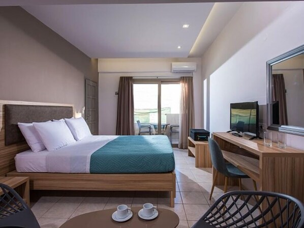 Habitación de hotel con cama, escritorio, silla, televisión y balcón con mesa y sillas.